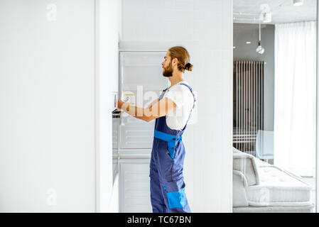 Handsome workman installing new refrigerator in the modern kitchen at home Stock Photo