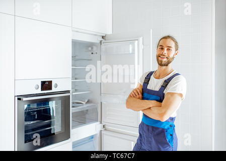Portrait of a handsome workman installing new refrigerator in the modern kitchen at home Stock Photo