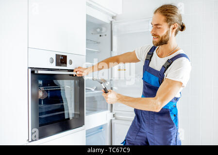 Workman checking the strength of the glass oven door with a hammer at home Stock Photo