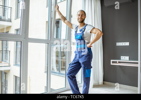 Portrait of a handsome workman in overalls standing near the window in the renovared apartment Stock Photo