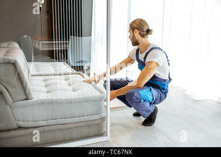 Handsome mover in uniform fixing sofa at the living room, delivering some furniture Stock Photo