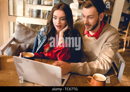 surprised man and beautiful young woman looking at laptop in cafe Stock Photo