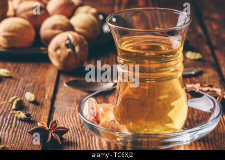 Spiced tea with star anise, cardamom and dried lime in oriental glass over wooden surface Stock Photo