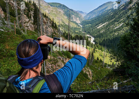 Young man with backpack on the top, taking a photo of mountains gorge. View from the back. Stock Photo