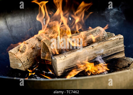 Burning logs flaming in a barbecue fire on a bed of hot coals in a close up view conceptual of an outdoor lifestyle and natural fuel Stock Photo