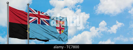 Angola and Fiji flag waving in the wind against white cloudy blue sky together. Diplomacy concept, international relations. Stock Photo