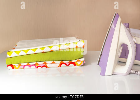 Iron and a stack of ironed linen lying on a white table Stock Photo