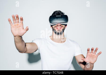 cheerful bearded man wearing virtual reality headset while gesturing on white Stock Photo