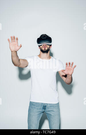 surprised bearded man wearing virtual reality headset while gesturing on white Stock Photo