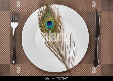top view fork and knife and a peacock feather on a dish concept of eating inhuman wildlife animal Stock Photo