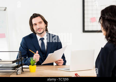 selective focus of handsome recruiter holding pencil and papers near brunette woman Stock Photo
