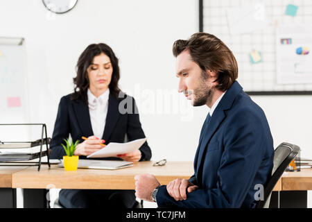 selective focus of handsome man sitting near attractive recruiter in office Stock Photo