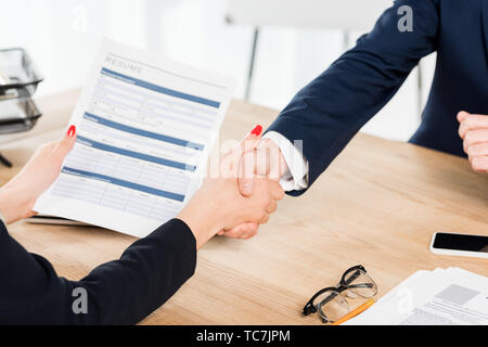 cropped view of recruiter holding resume and shaking hands with employee in office Stock Photo