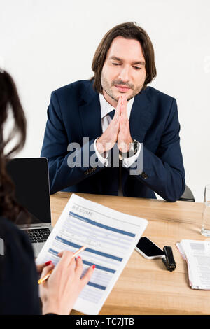 selective focus of handsome man sitting with praying hands near recruiter Stock Photo