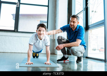 father helping smiling son with plank exercise at gym Stock Photo