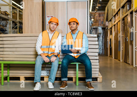 concentrated multicultural workers sitting on bench in warehouse Stock Photo