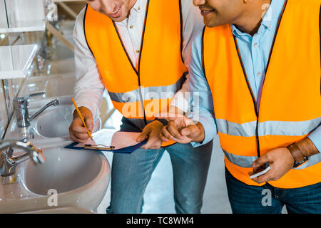 cropped view of multicultural colleagues in safety vests working in plumbing department Stock Photo