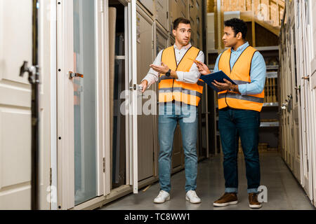 handsome multicultural storehouse workers talking while standing in doors department Stock Photo