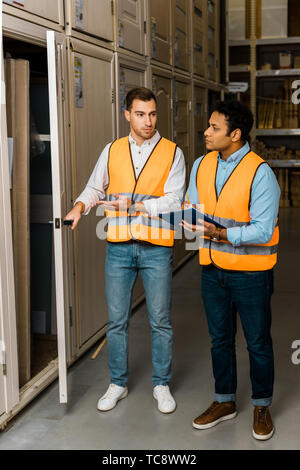 good-looking warehouse worker opening door near indian colleague Stock Photo