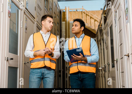 serious multicultural warehouse workers talking while standing in doors department Stock Photo