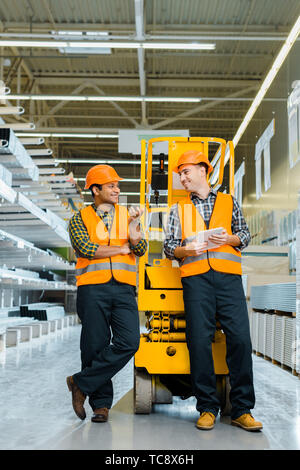 smiling multicultural workers talking while standing near scissor lift Stock Photo