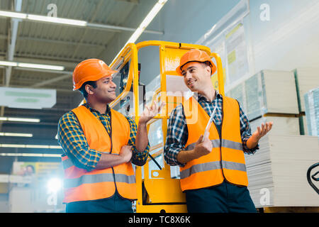 cheerful multicultural workers talking and gesturing while standing near scissor lift Stock Photo
