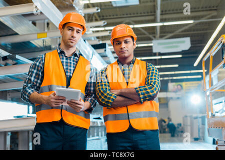 serious multicultural workers in safety vasts and helmets looking at camera Stock Photo