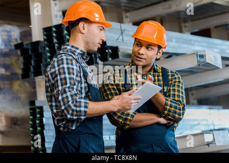 multicultural, concentrated warehouse workers talking while using digital tablet Stock Photo