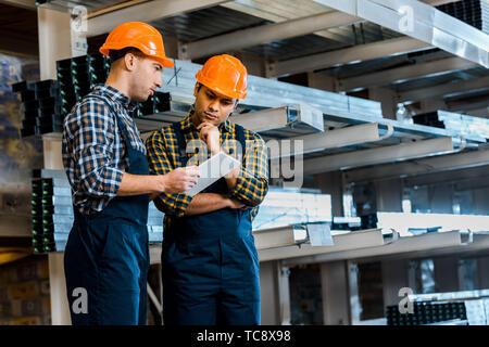 thoughtful multicultural warehouse workers in uniform using digital tablet Stock Photo