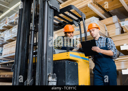 multicultural warehouse workers talking near forklift machine Stock Photo