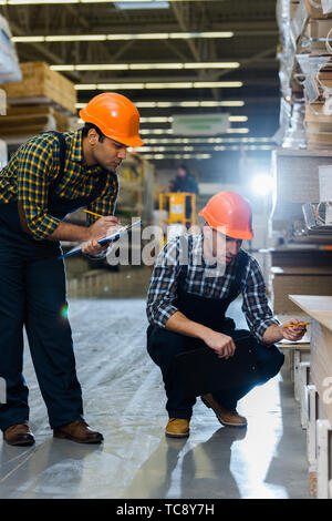 two multicultural colleagues in uniform and helmets working in warehouse Stock Photo