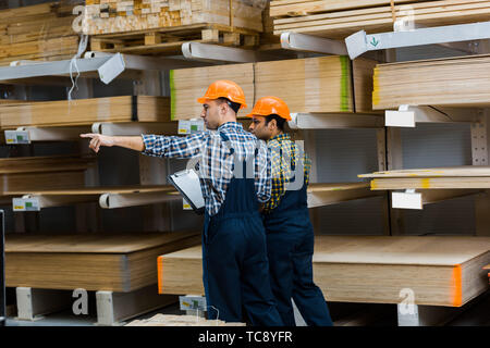 warehouse worker pointing with finger while standing near indian friend Stock Photo