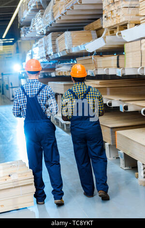 back view of two multicultural workers in overalls and helmets in warehouse Stock Photo