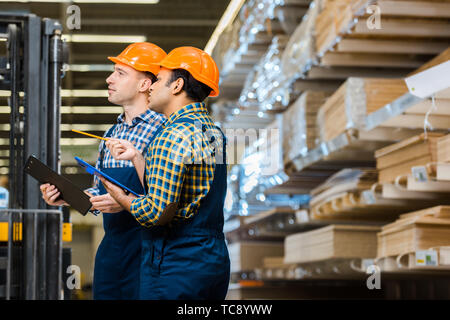 two multicultural workers in uniform smiling and holding clipboards Stock Photo