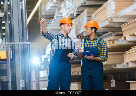 smiling worker pointing with pencil while talking to indian colleague Stock Photo