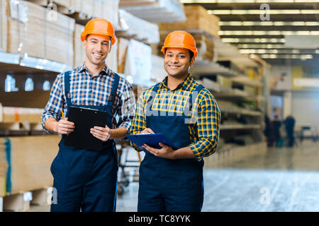 two multicultural workers in uniform smiling and looking at camera in warehouse Stock Photo
