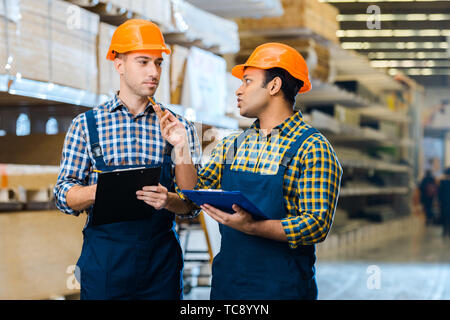 two serious multicultural warehouse workers talking and holding clipboards Stock Photo