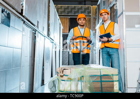 concentrated multicultural warehouse workers standing near pallet jack in warehouse Stock Photo