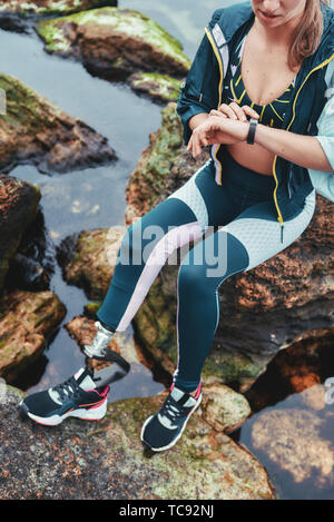 Checking results. Cropped photo of disabled athlete woman in sportswear with prosthetic leg checking pedometer while sitting on the stone. Disabled Sportsman. Healthy lifestyle. Sport concept Stock Photo