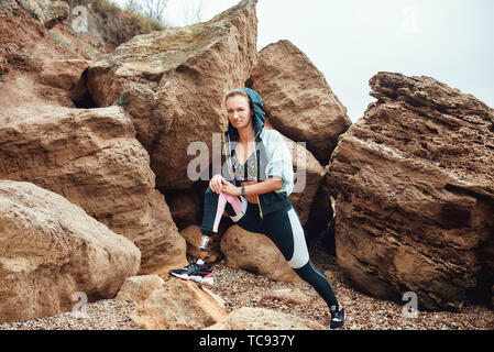 Sport is my way of life. Beautiful and young disabled athlete woman in sportswear with prosthetic leg standing on the beach after morning workout and looking at camera. Sport concept. Sport outside. Disabled Sportsman. Stock Photo