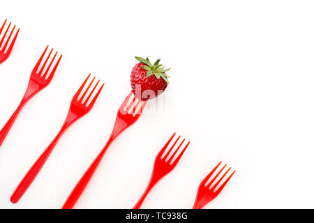 Straeberry and red plastic forks in row on white background with copy spase. Stock Photo