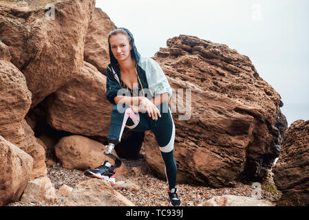 Never give up Beautiful and young disabled athlete woman in sportswear with prosthetic legs12n9g standing on the beach after morning workout and looking at camera. Sport concept. Sport outside. Disabled Sportsman. Stock Photo