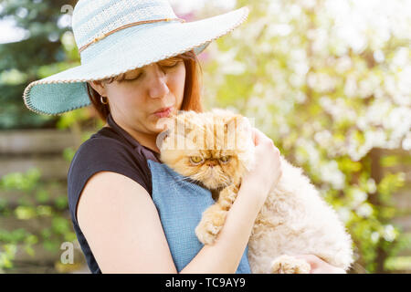 Picture of woman in hat with cat in hands on blurred background in garden Stock Photo