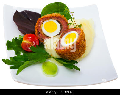 Hard-boiled quail egg wrapped in sausage meat, breaded and fried (Scotch egg) served with pureed potatoes, baked carrots, cherry tomatoes and greens. Stock Photo