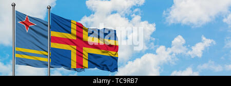 Aruba and Aland Islands flag waving in the wind against white cloudy blue sky together. Diplomacy concept, international relations. Stock Photo