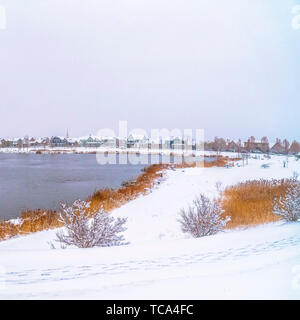 Frame Square Panorama of a silvery lake with snow covered shore and metal bridge Stock Photo