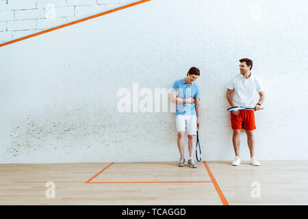 Full length view of smiling squash players in polo shirts Stock Photo