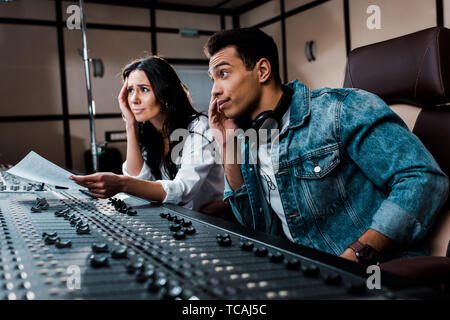 two thoughtful sound producers working at mixing console in recording studio Stock Photo