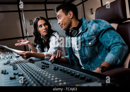 two quarrelling multicultural sound producers working at mixing console in recording studio Stock Photo