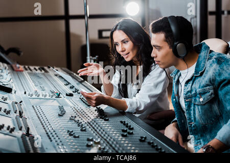 two young multicultural sound producers working at mixing console in recording studio Stock Photo